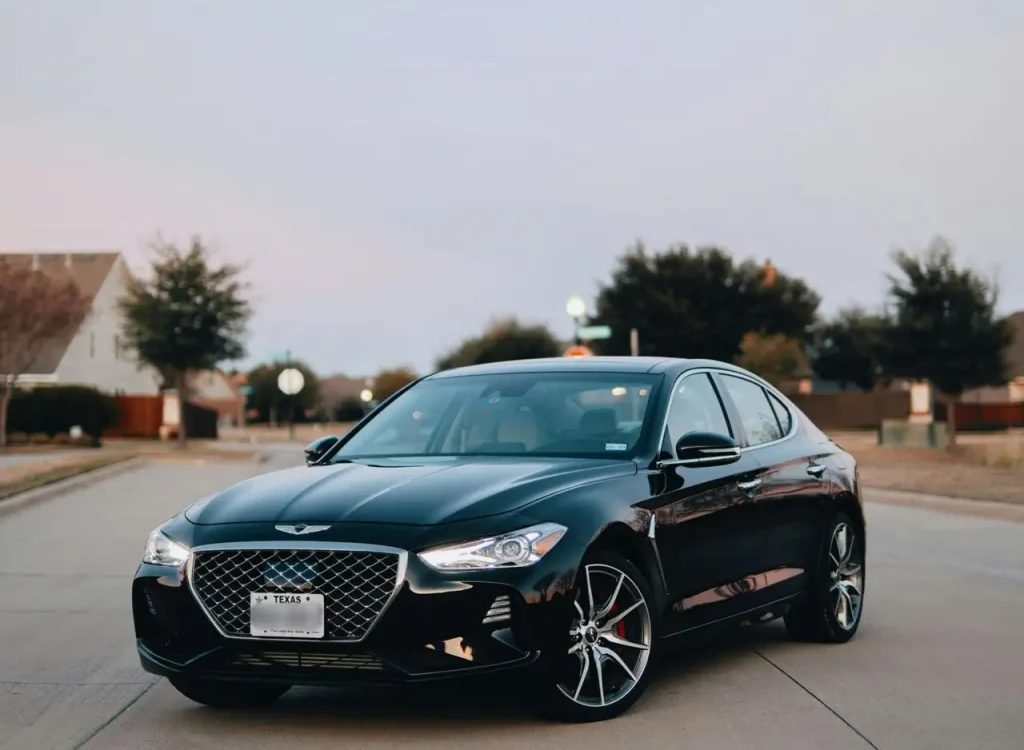 Luxury black sedan with shining headlights parked on a suburban road during daytime.
