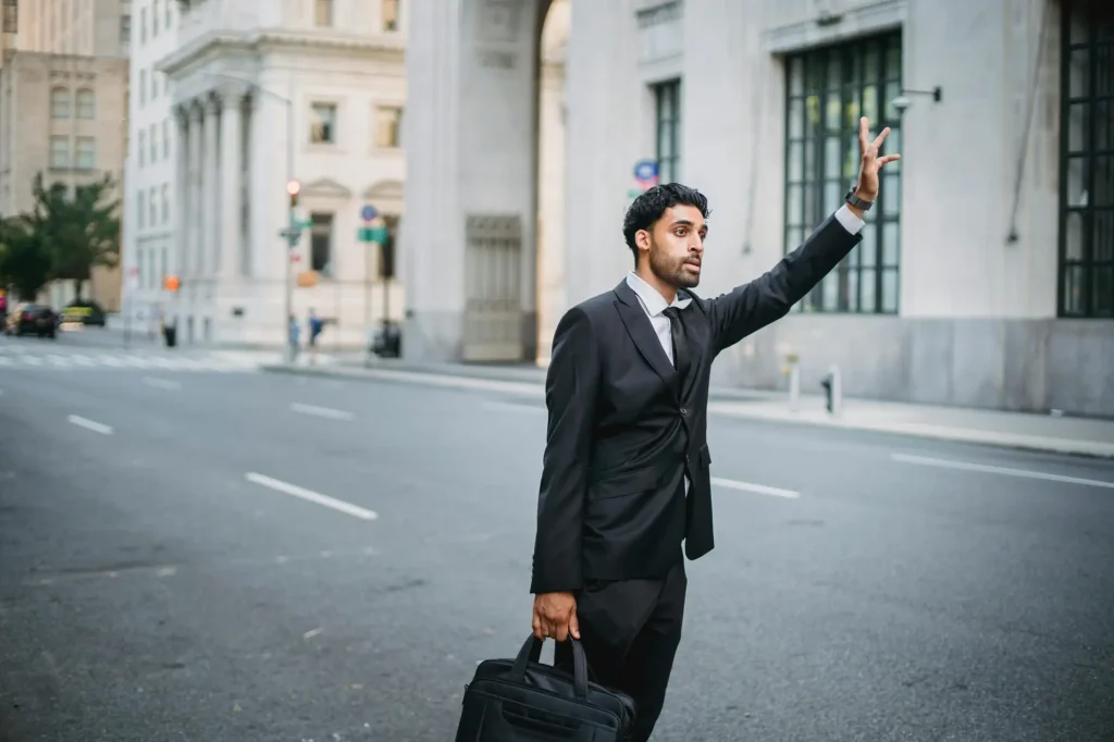 Businessman in formal attire hailing a taxi on a city street with elegant architecture.