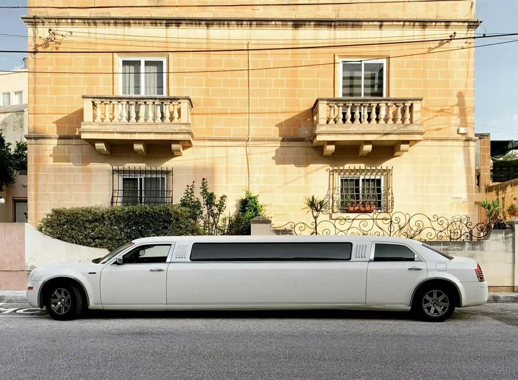 A sleek white limousine parked in front of a classic Maltese house in San Ġwann.